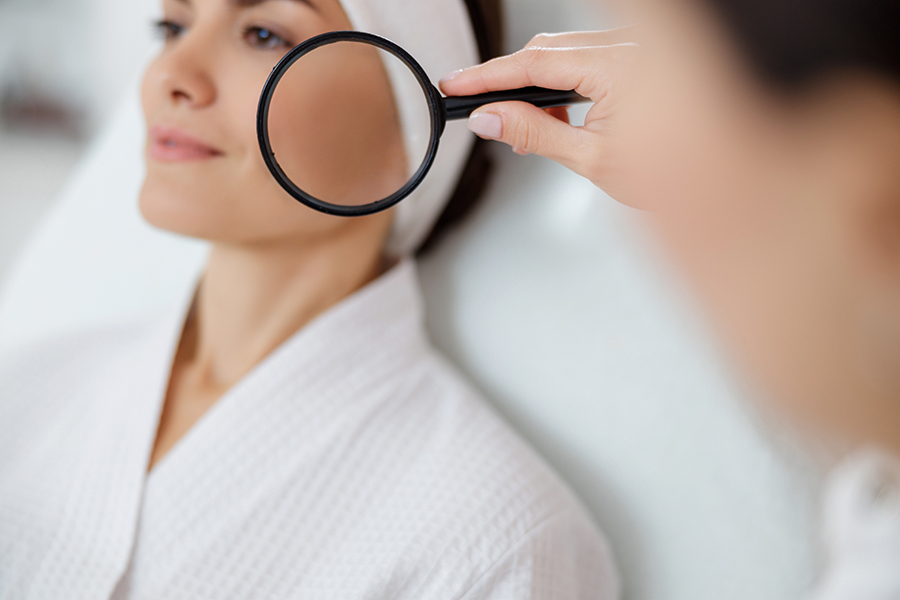 Beautician examining lady skin with magnifying glass