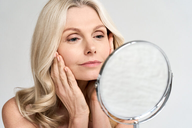 Closeup portrait of gorgeous happy middle aged woman looking at mirror touching her skin