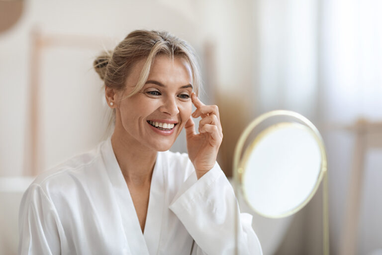 Cheerful beautiful adult lady using moisturizing eye cream