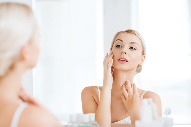 Happy young woman checking her chin and neck in the mirror