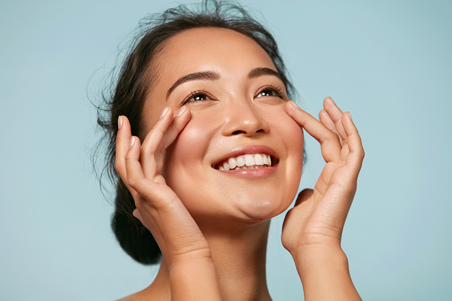 Beautiful smiling asian girl model with natural makeup touching glowing hydrated skin