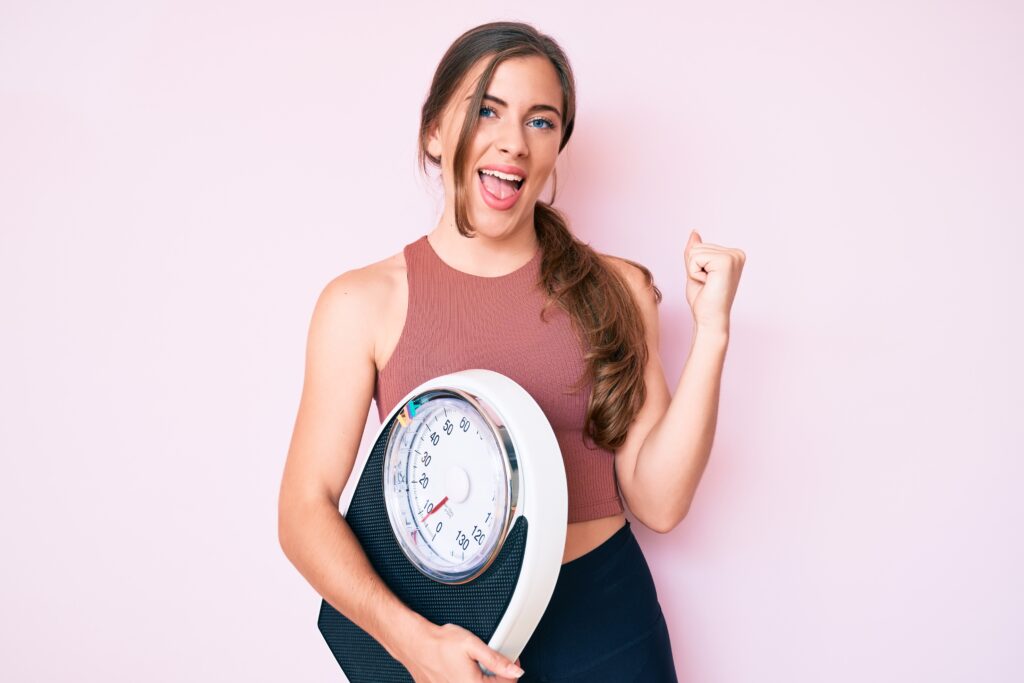 Weight Loss Treatments 3 Beautiful Young Caucasian Woman Holding Weight Machine To Balance Weight Loss Screaming Proud, Celebrating Victory And Success Very Excited With Raised Arms
