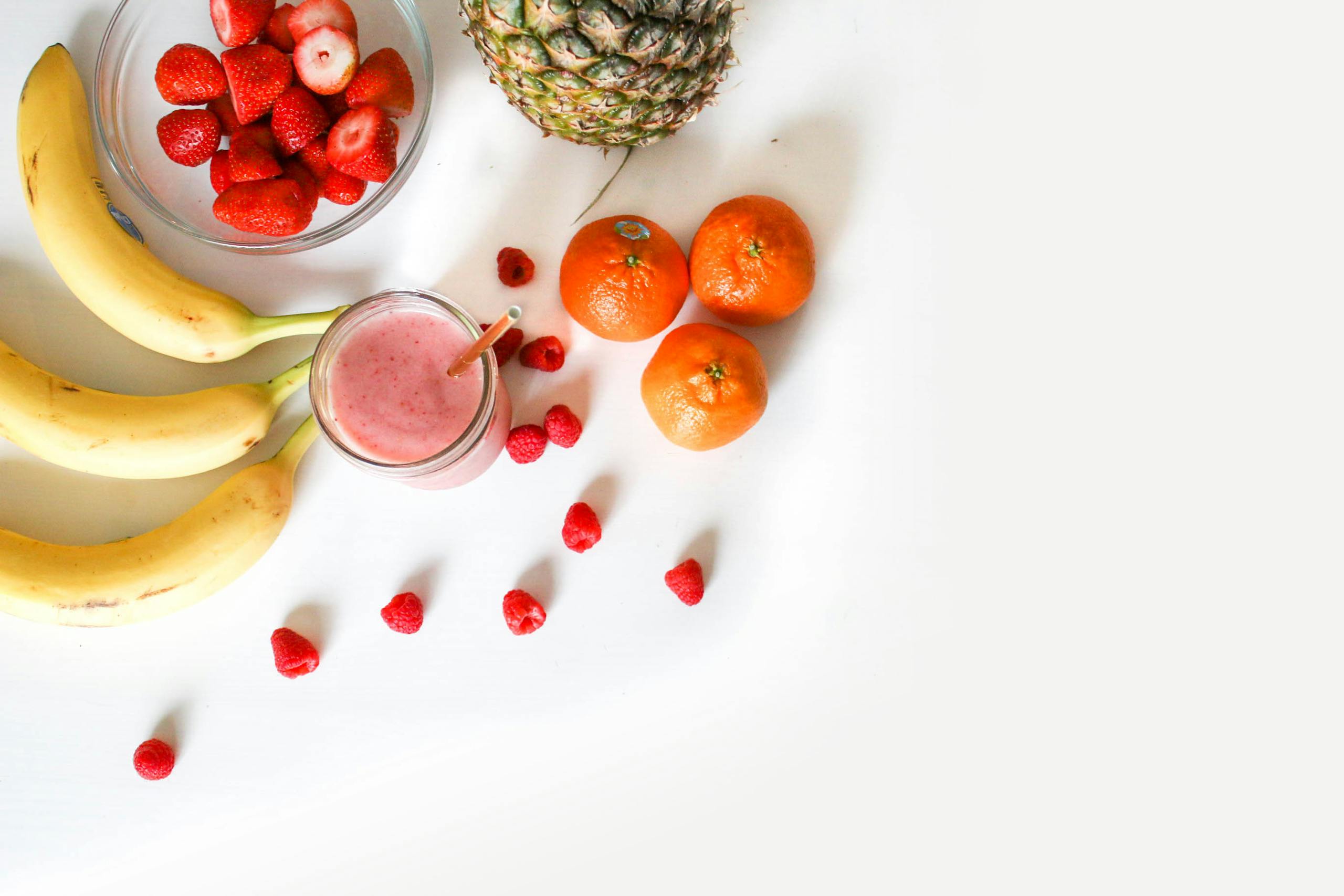 Wellness 7 A Vibrant Flat Lay Of Tropical Fruits Including Bananas, Strawberries, And A Smoothie On A White Background.